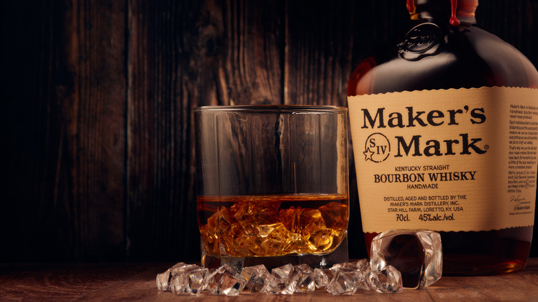 Bottle of Maker's Mark kentucky straight bourbon whisky handmade and glass with drink and ice standing on a wooden table on wooden background with copy space.