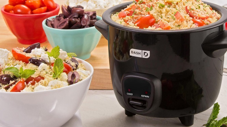 A Dash mini rice cooker full of food and surrounded by ingredients on a wood board