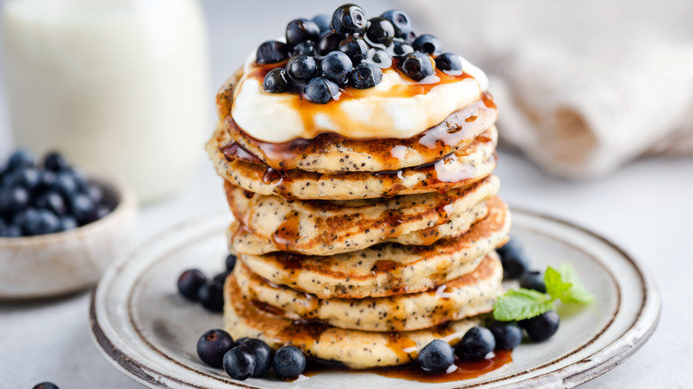 stack of poppy seed pancakes with blueberries, syrup, and cream cheese