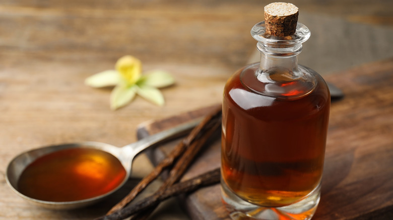 small bottle of vanilla extract with vanilla beans and measuring spoon of extract