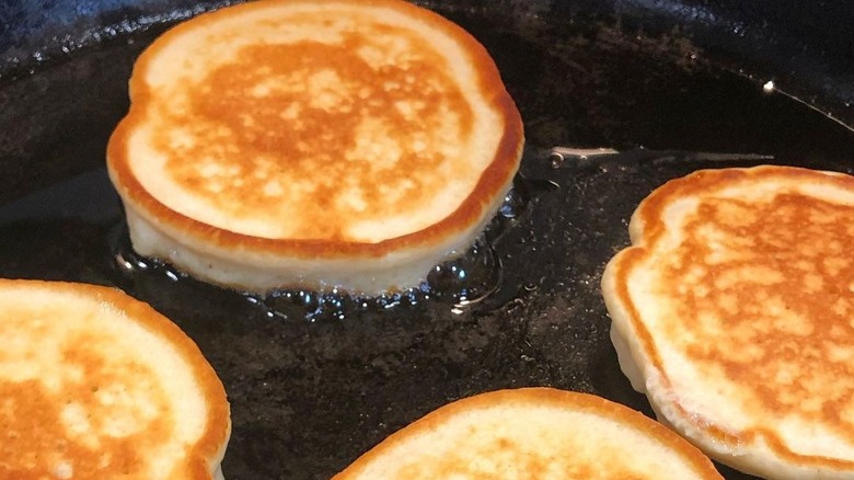 close up of golden brown pancakes cooking in an oiled cast iron skillet