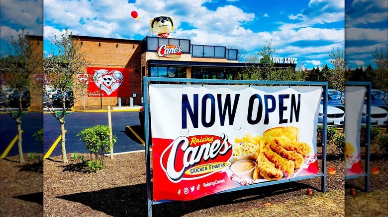 Exterior of a Raising Cane's restaurant with a "Now Open" sign in front