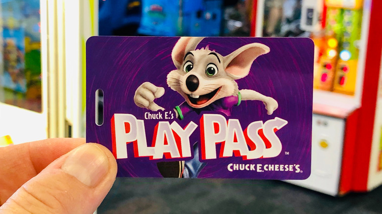 hand holding Chuck. E. Cheese play pass with arcade in background