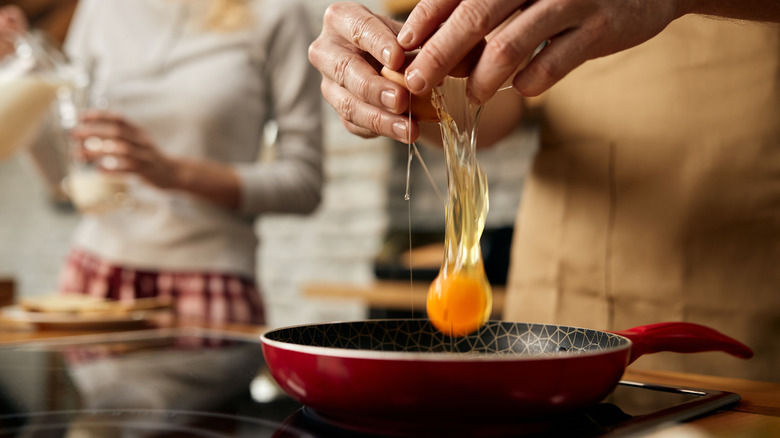 person cracking egg into pan