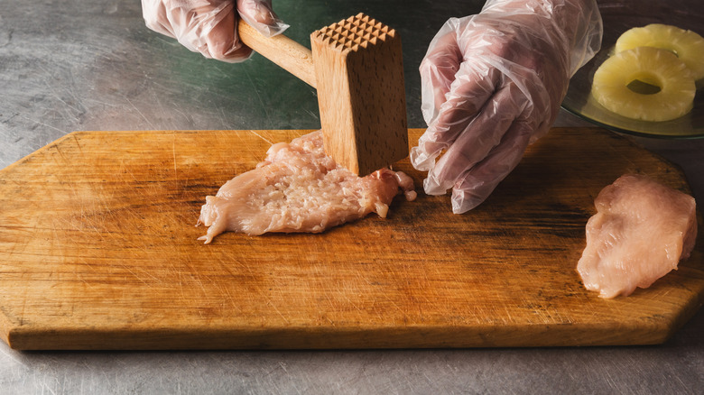 person tenderizing chicken