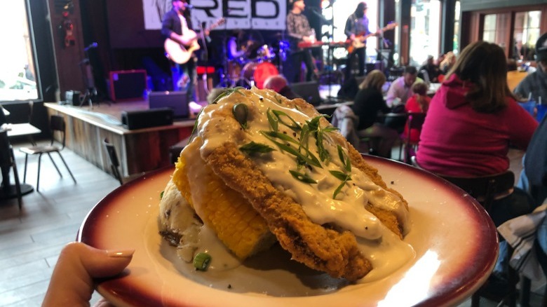 platter of mashed potatoes topped with corn on the cob and chicken fried steak while band plays in the background