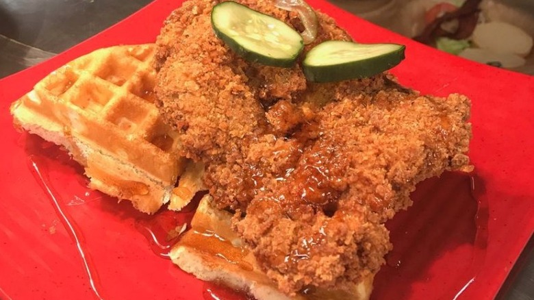 hot chicken and waffles on red plate with syrup and pickles