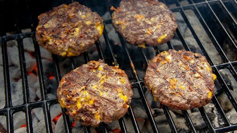 four burgers being grilled on a charcoal grill