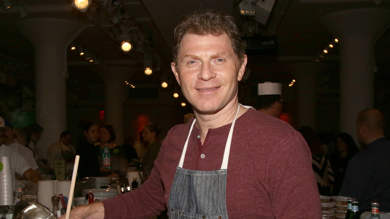 Bobby Flay smiling while wearing chef's apron and stirring pot
