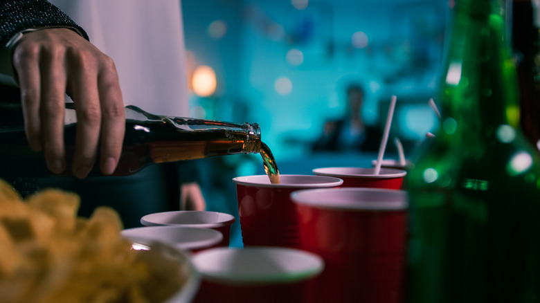 Person at dim-light party pouring beer into red cup