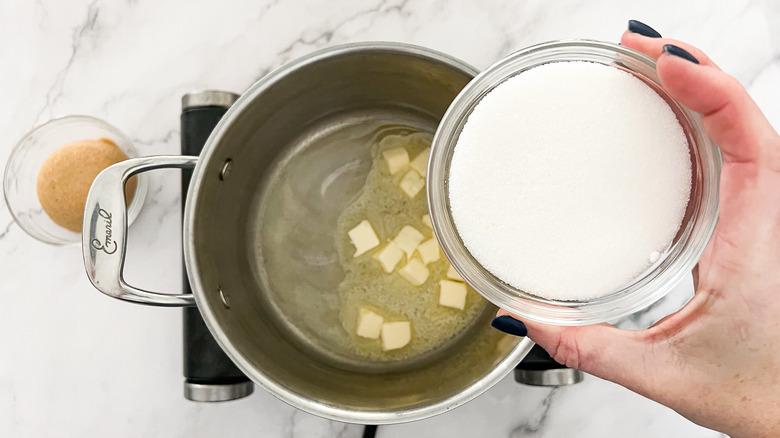 hand adding sugar to pan