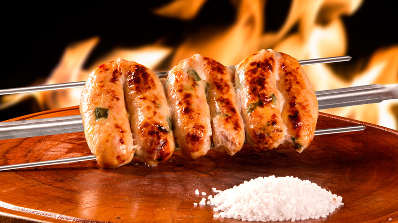 brazilian sausages on wooden slab next to salt in front of fire