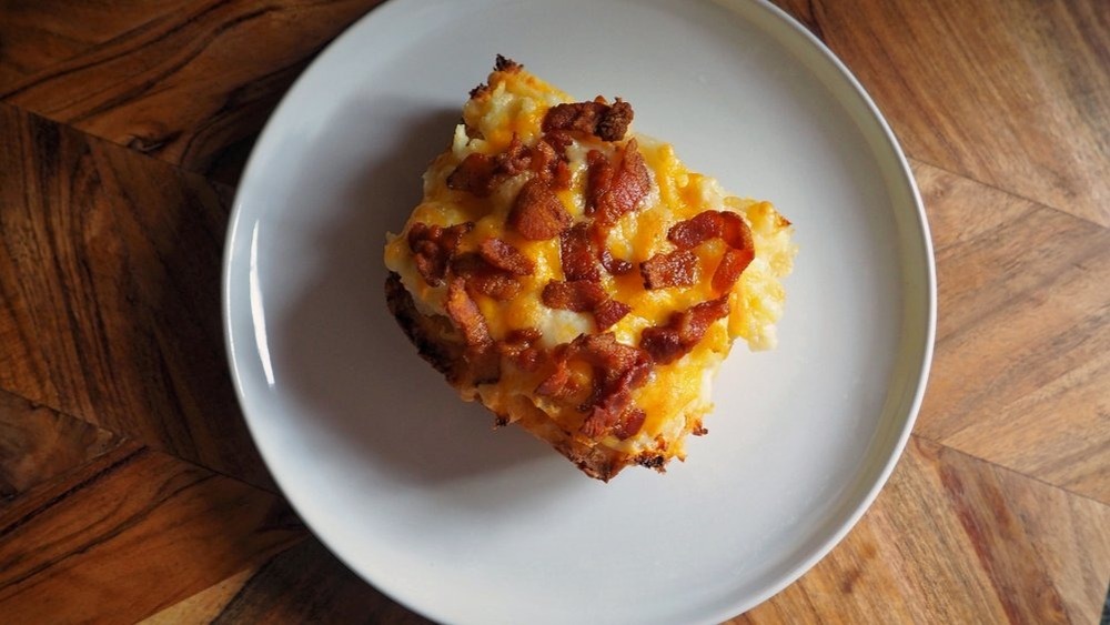 loaded hashbrown casserole with cheese and bacon on a white plate on a wooden table