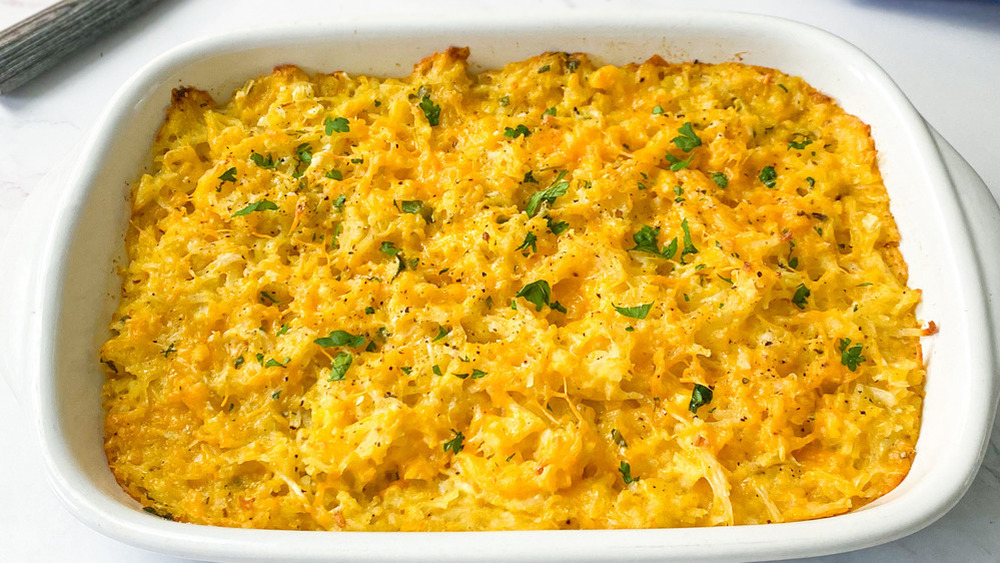 Cheesy hashbrowns topped with parsley in a white casserole dish on a white counter