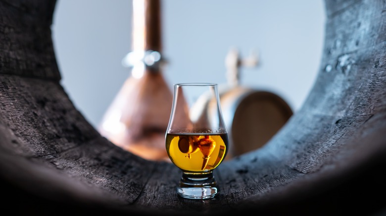 Single glass of whiskey in a barrel with blurry machinery in the background