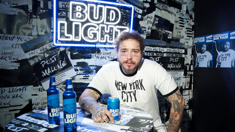 Post Malone seated at a table with cans of Bud Light