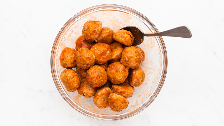 Tossing chicken meatballs with buffalo sauce in bowl