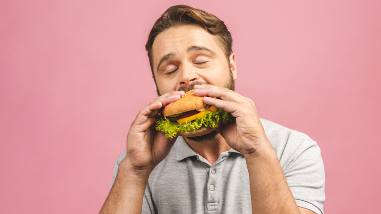 man biting burger on pink background