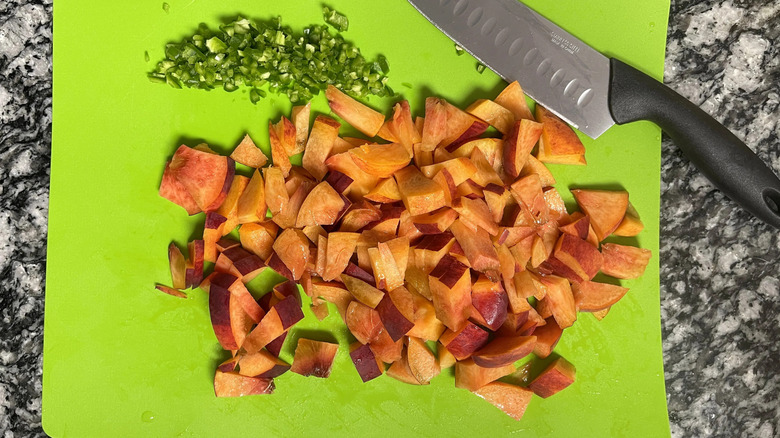 Chopped peaches and jalapeno on cutting board with knife