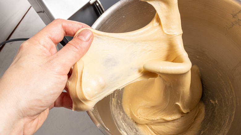 Stretching a dough for a windowpane test on the hook of a stand mixer