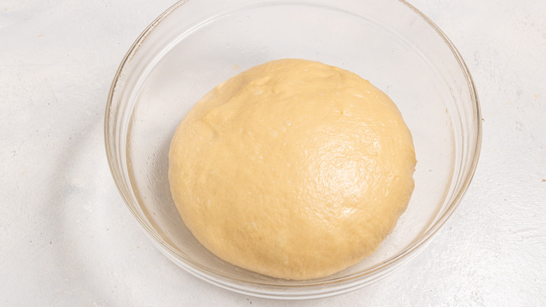 Dough shaped into a ball inside a glass bowl