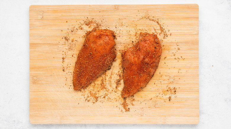 Spice-covered chicken breasts on wooden cutting board