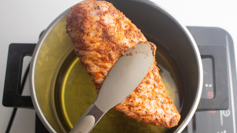 Tongs holding a turkey wing above a pot of oil