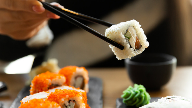 Hand holding sushi with chopsticks