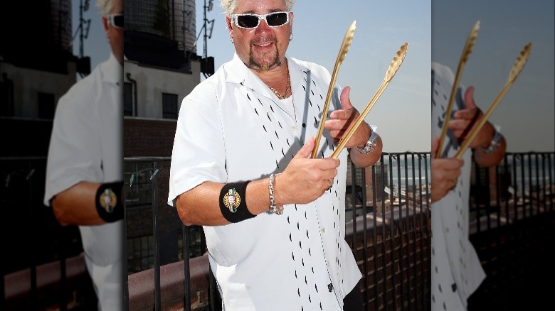 Guy Fieri holding gold tongs