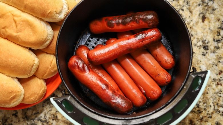 Hot dogs in air fryer with plated buns on side