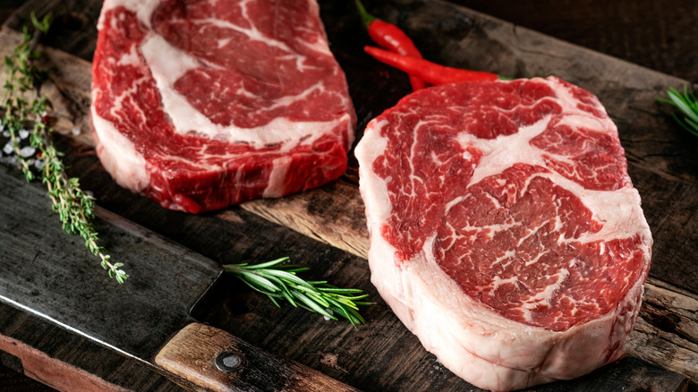 Raw steaks and herbs on cutting board