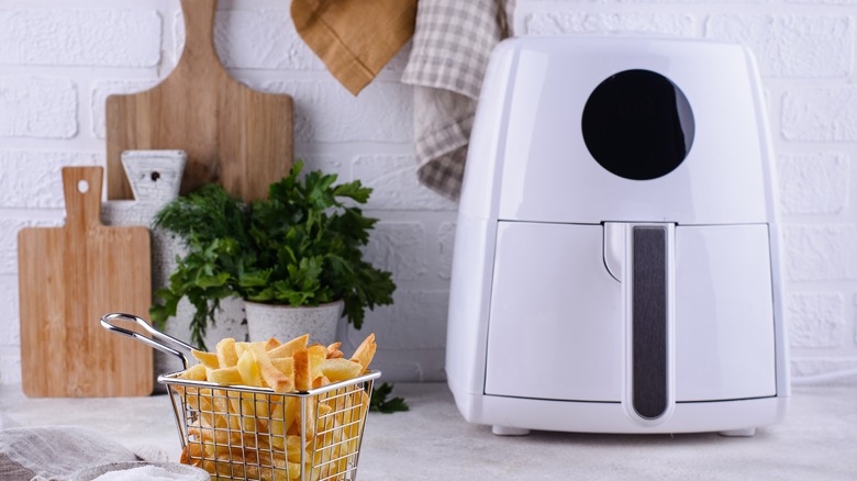 Air fried chips in a basket next to a white air fryer 