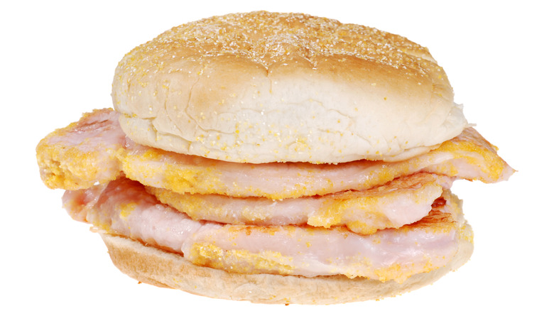 A bun filled with peameal bacon against a white background