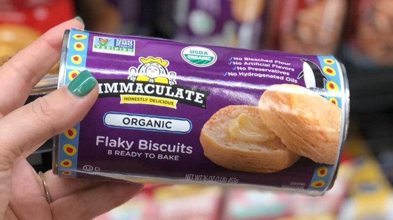 A hand holding a can of immaculate organic flaky biscuits