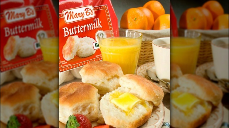 Freshly baked biscuits on a plate in front of a bag of mary B's buttermilk biscuits with orange juice at ta breakfast table
