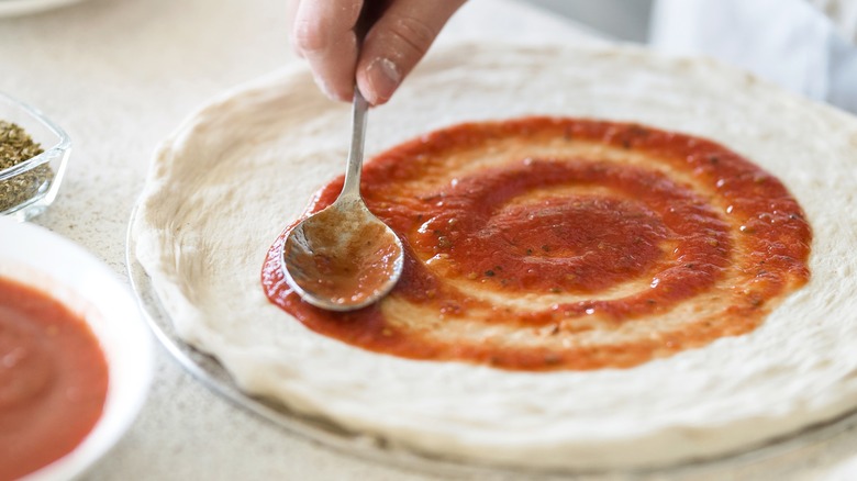 hand spreading sauce on pizza