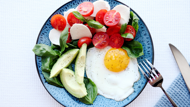 A fried egg with caprese salad and avocado