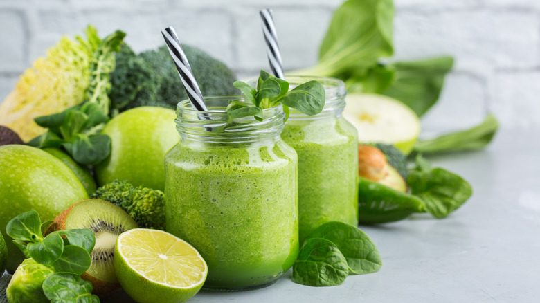 Two glasses of green smoothie surrounded by vegetables