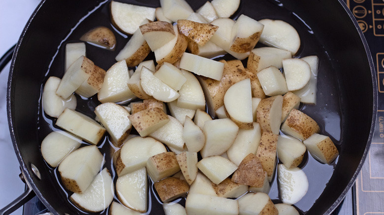 Overhead shot of sliced potatoes cooking in a skillet on the stove