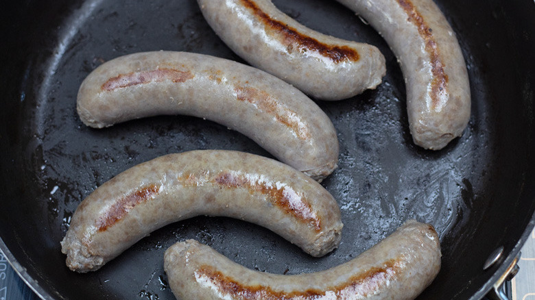 Five bratwursts (slightly browned) cooking in a skillet on the stove