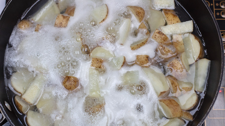 Overhead shot of sliced potatoes in bubbling water cooking in a skillet