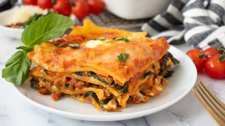 lasagna on a white plate surrounded by tomatoes and black-striped napkins