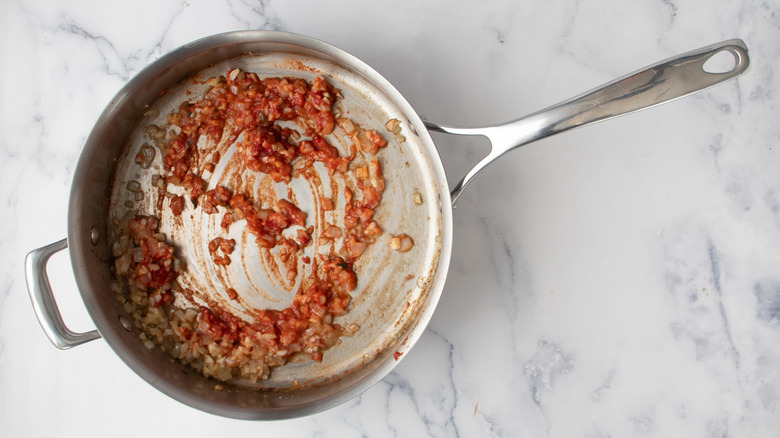 chopped onions and garlic in a frying pan with reddish paste