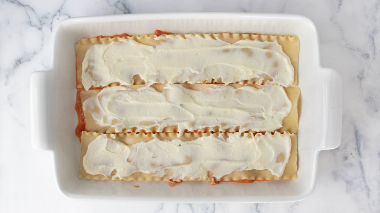 lasagna noodles covered with white paste in a white baking pan