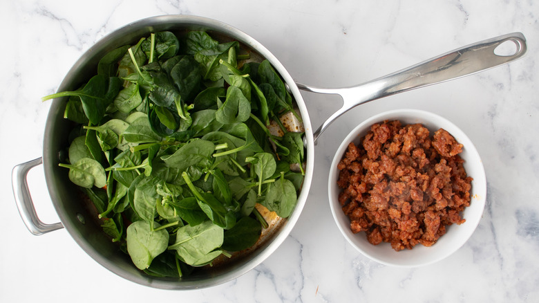 raw spinach in a frying pan and cooked ground meat in a white bowl