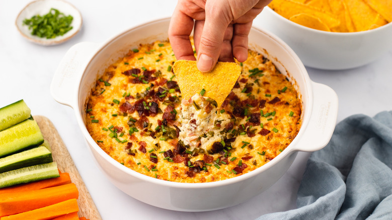 Dipping tortilla chip into cheesy bacon jalapeño dip