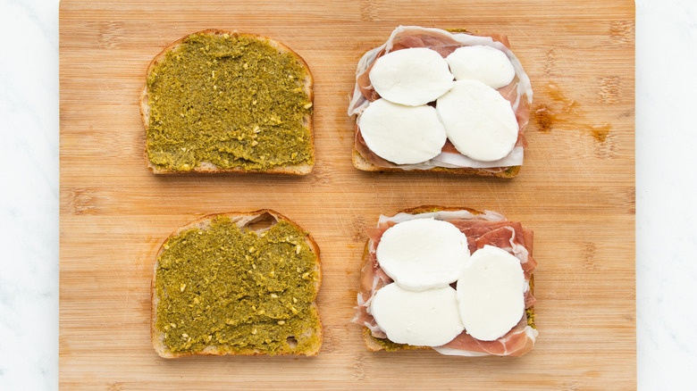 Bread on board with pesto, prosciutto, and mozzarella