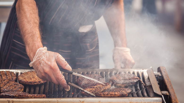 Person cooking burgers on a black grill