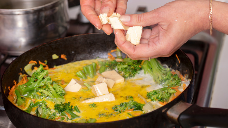 hands breaking cheese into skillet of broccoli cheese soup