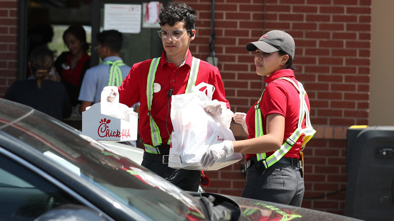 Chick-fil-A drive-thru workers holding bags of food next to car